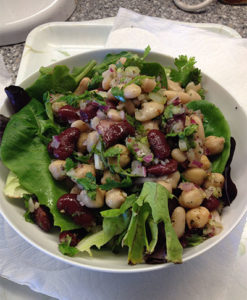 three bean salad in a white bowl with green garnish